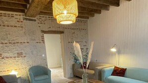 Ein gemütliches Wohnzimmer mit Steinboden, Holzbalkendecke und einer Pendelleuchte. Zwei Sofas, ein Couchtisch und eine Lampe sind vorhanden.