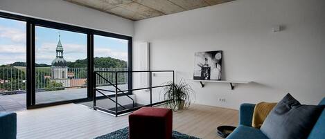 Una sala de estar moderna con un ventanal grande, un reposapiés rojo, un sofá azul y una obra de arte blanco y negro en la pared.