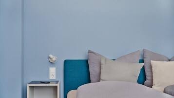 A bedroom with a bed, pillows, a nightstand, and a wall socket.
