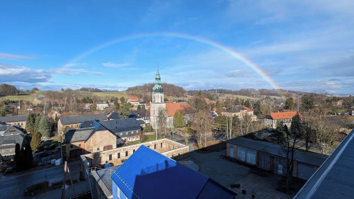 Une ville où se dresse une église imposante et où un arc-en-ciel illumine le ciel.