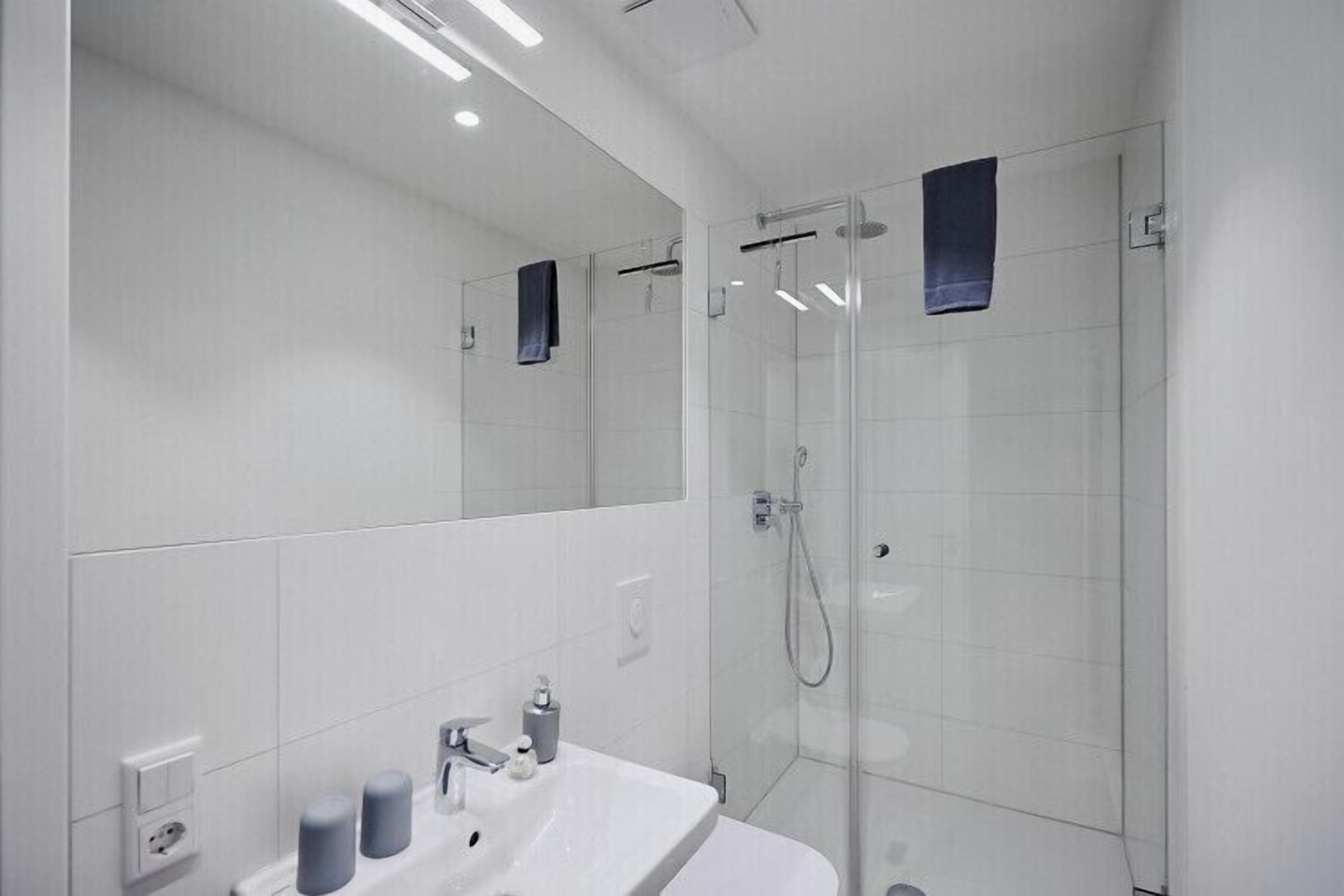 Un baño moderno con un espejo grande, un lavamanos y una ducha con cerramiento de vidrio.