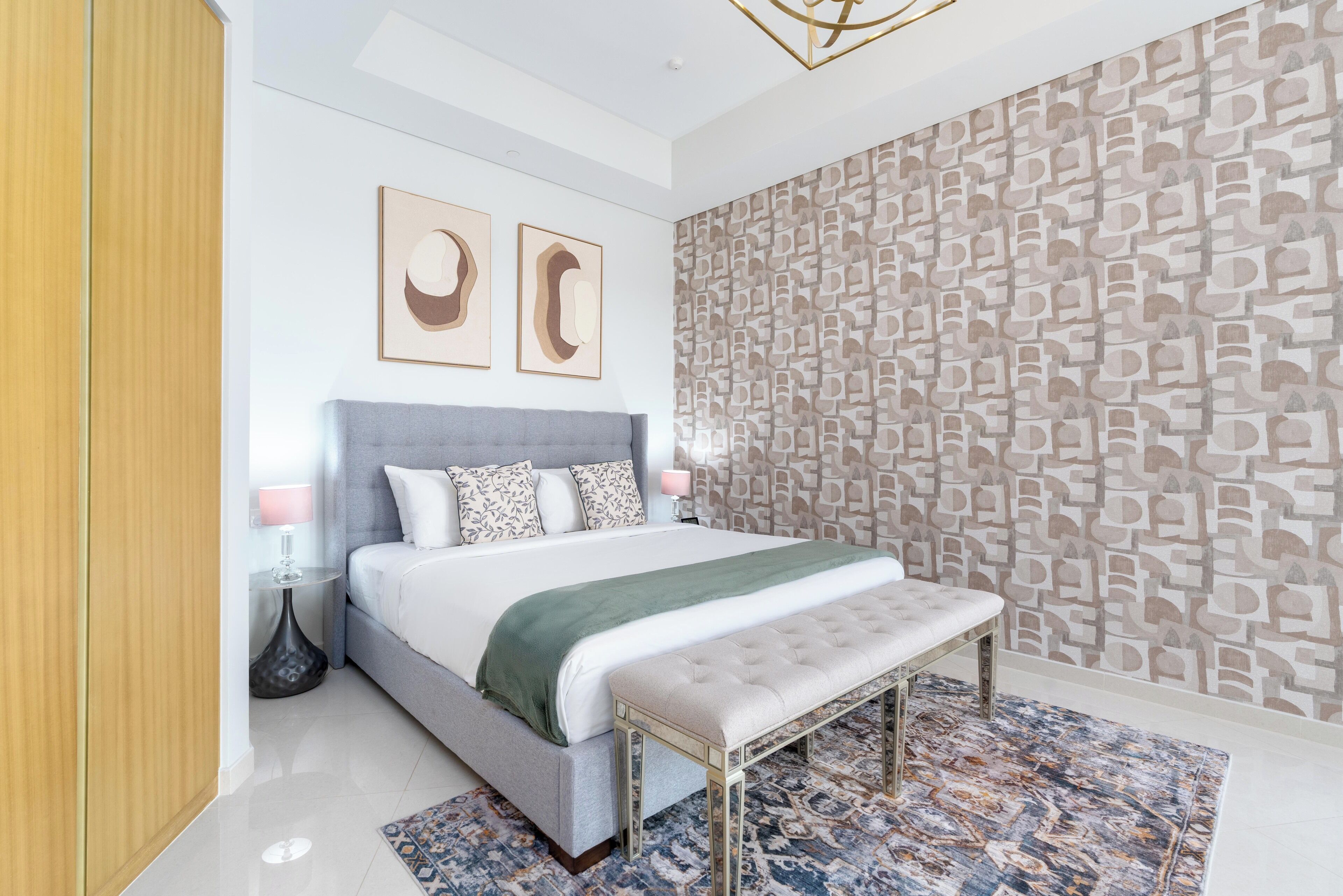 A modern bedroom with a large bed, a bench, patterned wallpaper, and two wall art pieces.