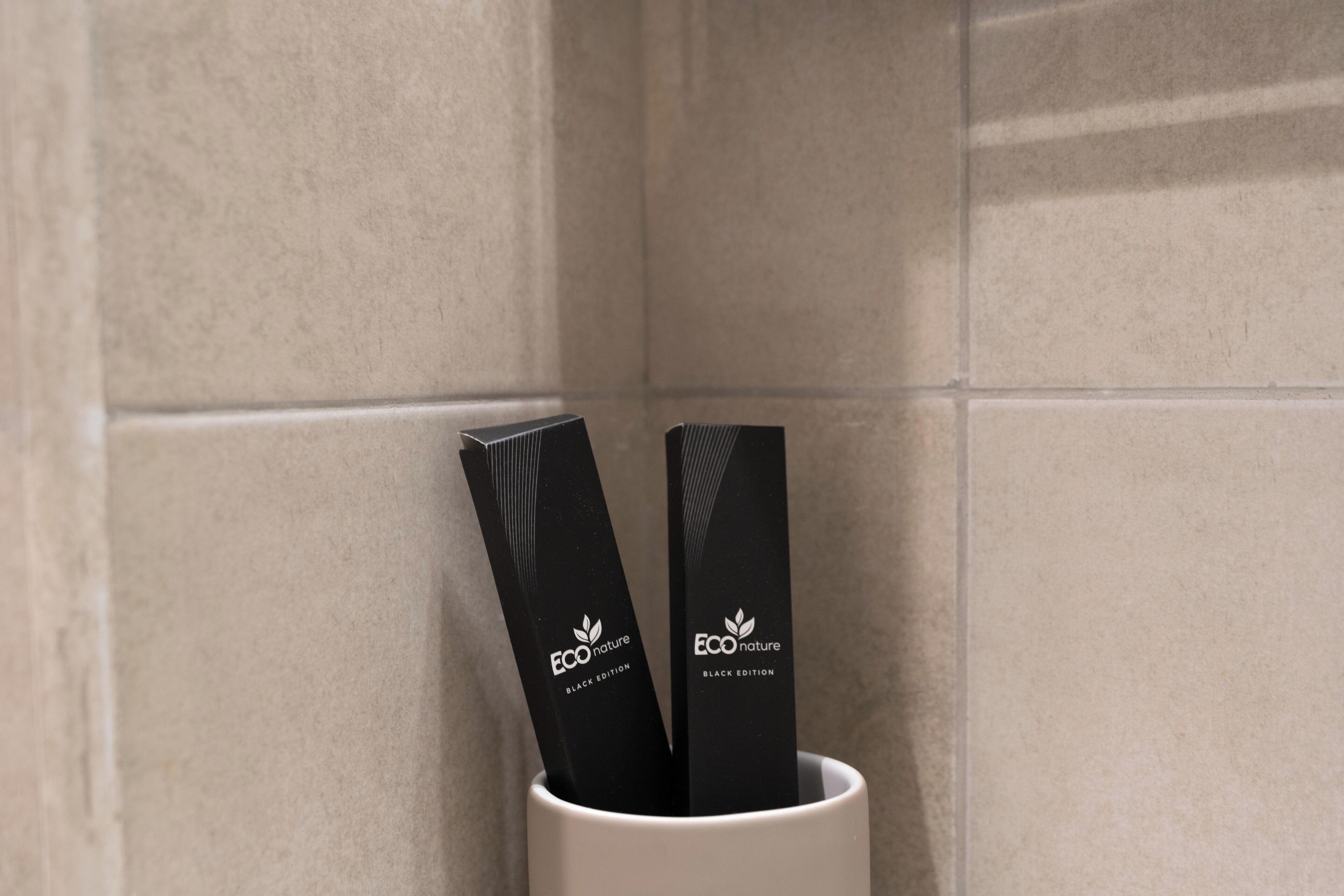 Two black EcoNature branded items in a white cup against a tiled wall.