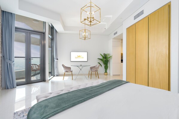 A modern bedroom with a large bed, a dining table with chairs, a potted plant, and a view of the outdoors.