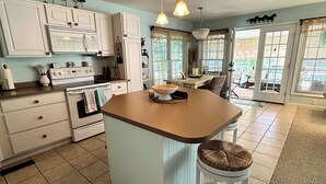 Une cuisine avec des meubles blancs, un îlot central doté d’un tabouret, un four à micro-ondes et une cuisinière.