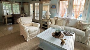 Un salon spacieux avec un ventilateur de plafond blanc, un canapé blanc, un fauteuil blanc et une table basse blanche.