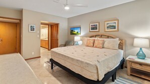 Une chambre à coucher comprenant un lit, une table de chevet, une lampe, un ventilateur de plafond et une porte donnant sur une autre pièce.