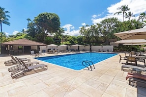 A swimming pool with lounge chairs and umbrellas, surrounded by palm trees and a clear sky.
