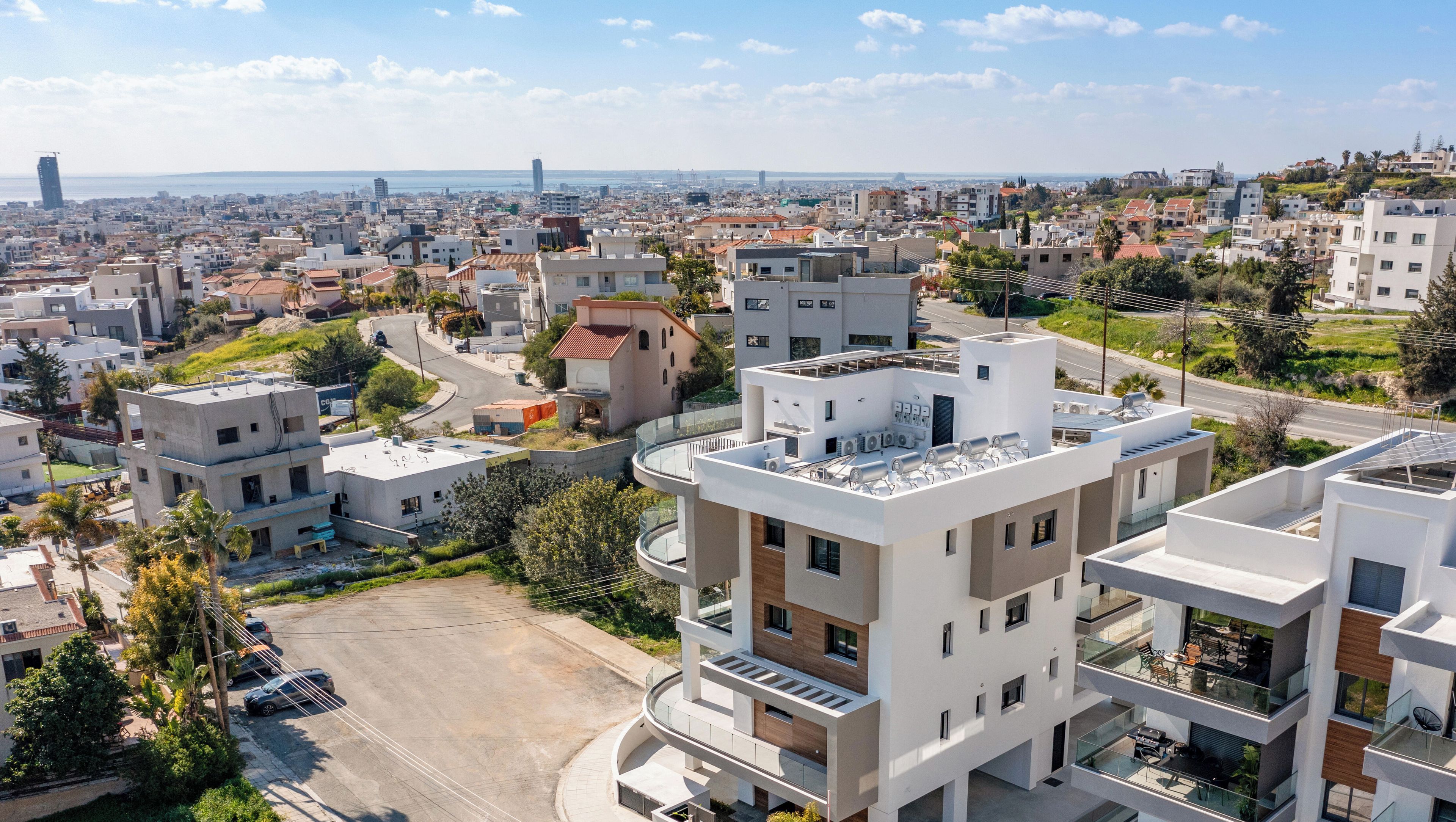 Una zona residencial moderna con edificios de varios pisos, una calle sinuosa y una vista despejada del horizonte urbano al fondo.