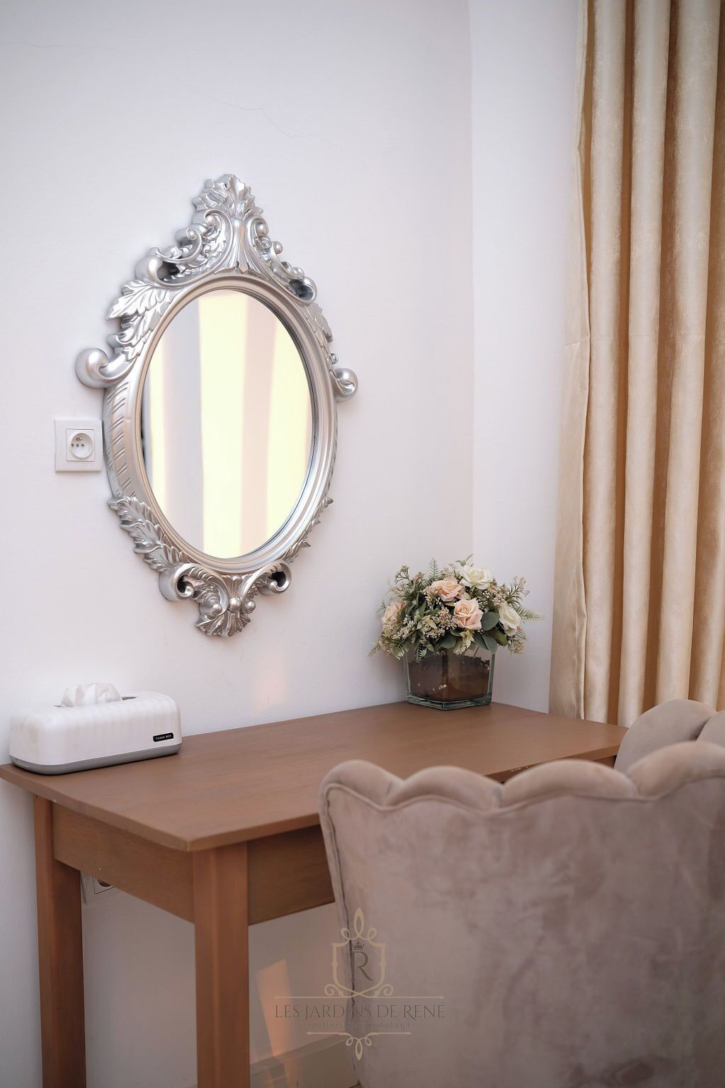 A room with a wooden table, a decorative mirror, a tissue box, and a vase with flowers.