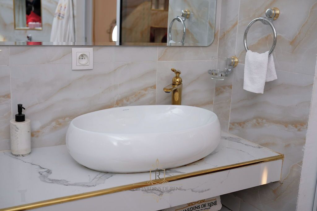 Un bagno con lavandino in marmo bianco, rubinetto dorato e porta asciugamani.