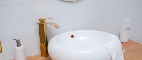 A bathroom with a white sink, gold faucet, and a white towel. - Les Jardins de René Villa (Yaoundé)