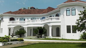 A large, white, two-story building with a red-tiled roof, a central courtyard, and a well-maintained lawn. - Les Jardins de René Villa (Yaoundé)