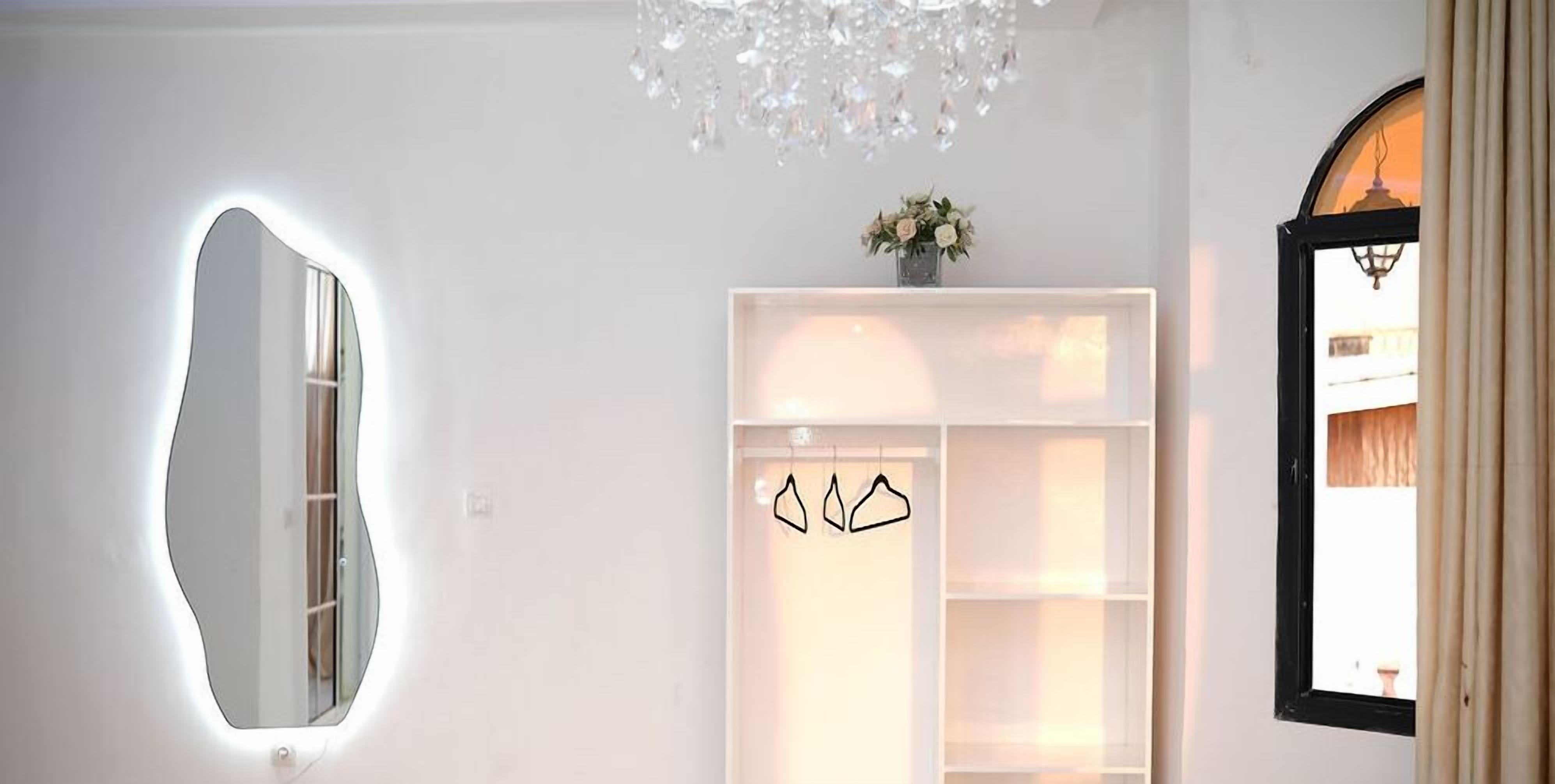 A modern interior with a unique mirror, a chandelier, and a minimalist shelving unit.