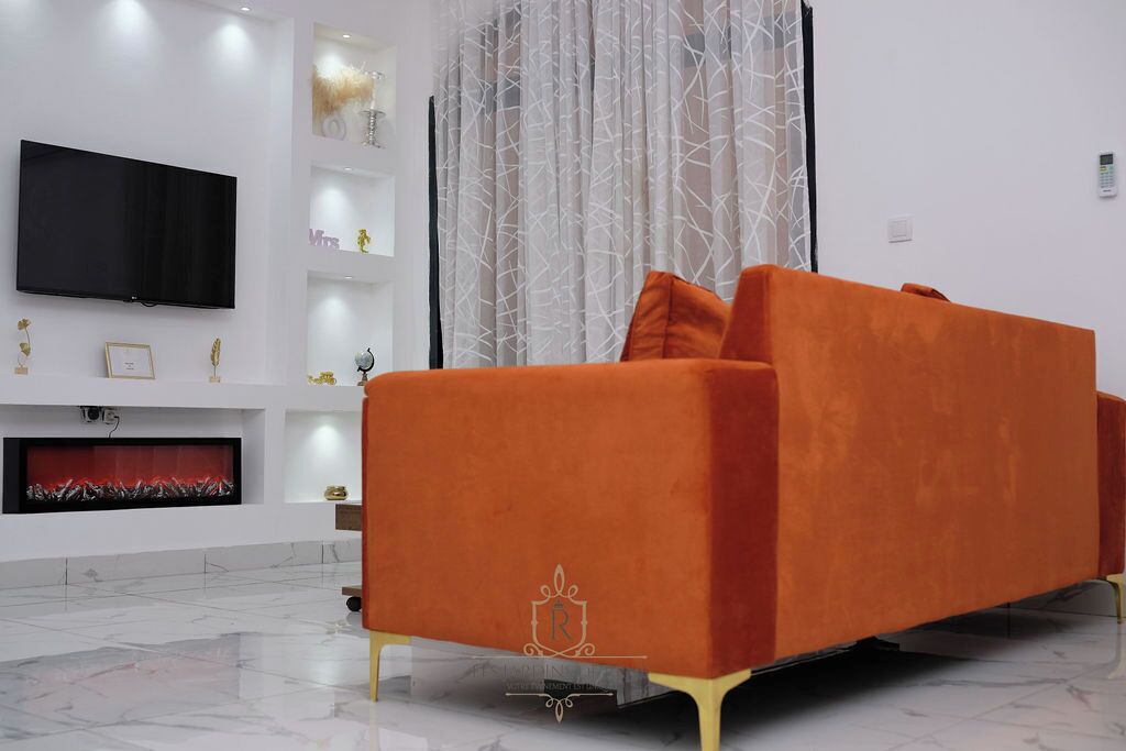 A modern living room with a large flat-screen TV mounted on the wall, a vibrant orange sofa, and a fireplace with a red fire.