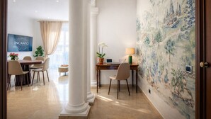 Et hotelværelse med spiseplads, et skrivebord med lampe, et fjernsyn og et mural på væggen.