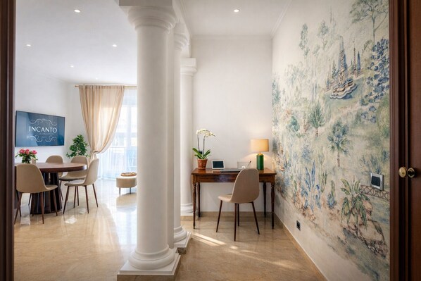 A hotel room with a dining area, a desk with a lamp, a television, and a mural on the wall. - Incanto House - Luxury apartment near the Vatican (Roma)