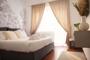 A neatly made bed with folded towels, a bedside table with a vase, and a window with curtains. - Incanto House - Luxury Apartment Near the Vatican (Roma)
