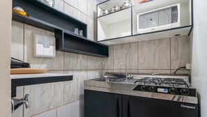 A compact kitchen with a gas stove, a microwave, and a sink. - AP 37 Ala Canto Gran Residencial Solavir (Bombinhas)