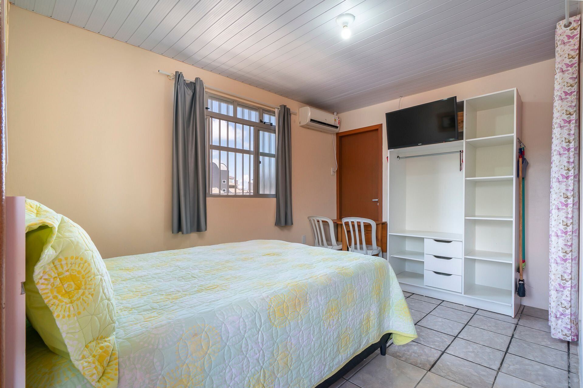 Ein Schlafzimmer mit Bett, einem Fenster mit Vorhängen, einem Kleiderschrank und einem Schreibtisch mit Stühlen.
