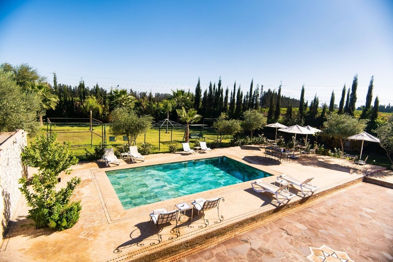 Ein rechteckiger Pool mit klarem Wasser, umgeben von einer Steinterrasse. Liegestühle und Sonnenschirme befinden sich im Poolbereich.