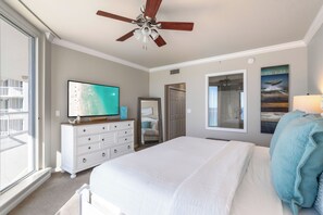 Une chambre avec un grand lit, un ventilateur de plafond, une télévision, une commode et une fenêtre donnant sur un balcon.