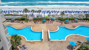 A resort with a large swimming pool, beach area with sun loungers, and a view of the ocean.