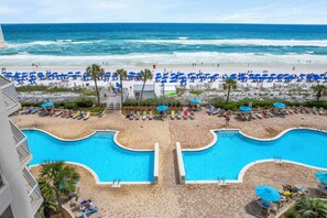 Un complexe hôtelier doté d’une grande piscine, d’une plage avec des chaises longues et offrant une vue sur l’océan.