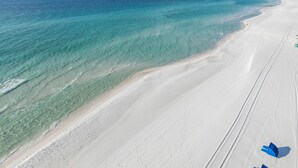 An aerial view of a beach with clear turquoise waters and a wide sandy shore.