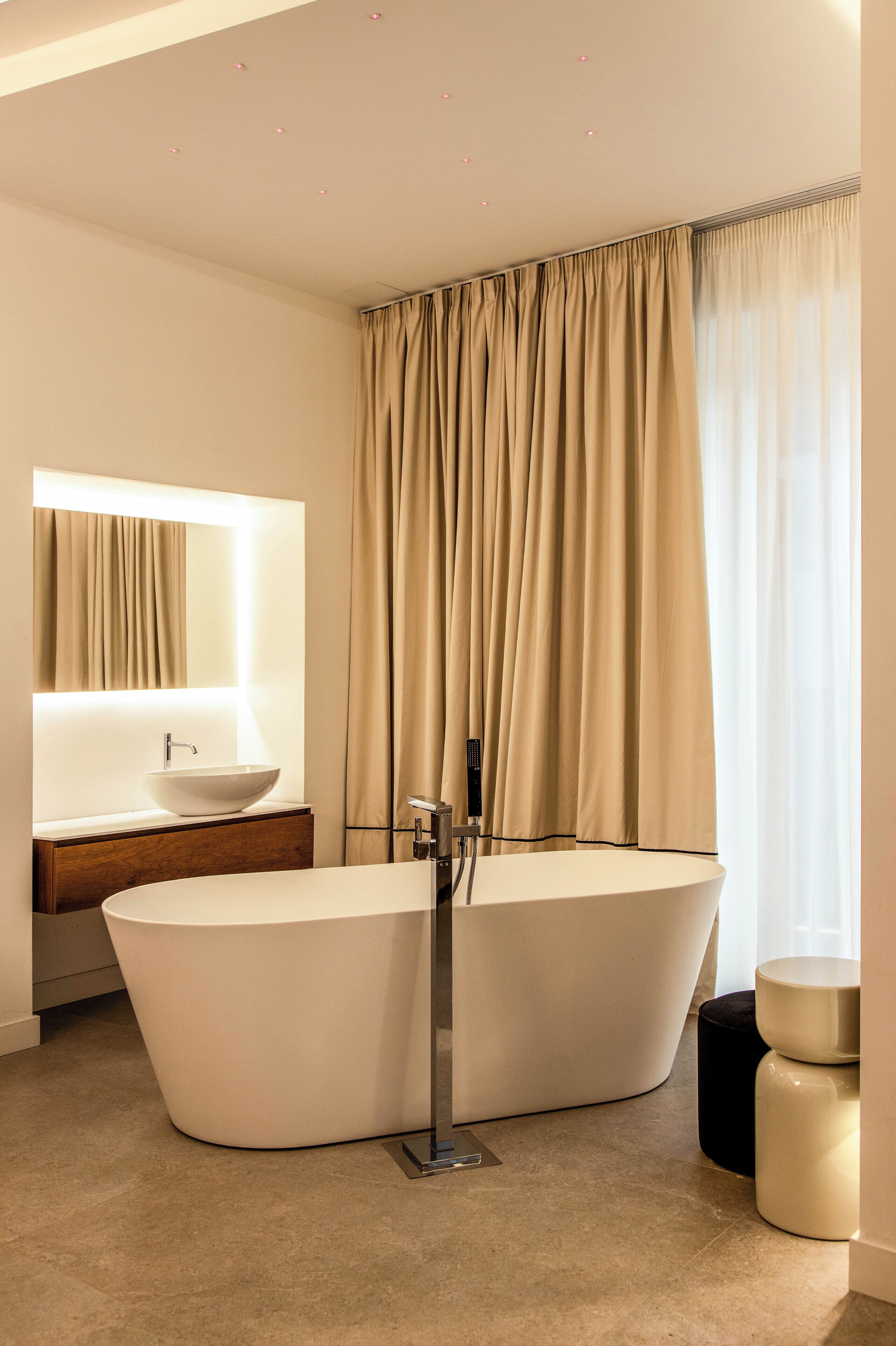 A modern bathroom with a freestanding bathtub, a vanity with a mirror, and a large window with curtains.