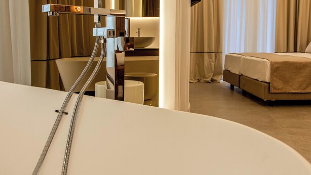 A modern hotel room with a large bathtub, a shower with a handheld hose, a bed, and a large mirror. - Mamalu - Corso Umberto (Naples)