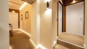 A hotel hallway with carpeted floors, wooden paneling, and a staircase leading to a door with a number plate. - Mamalu - Corso Umberto (Naples)