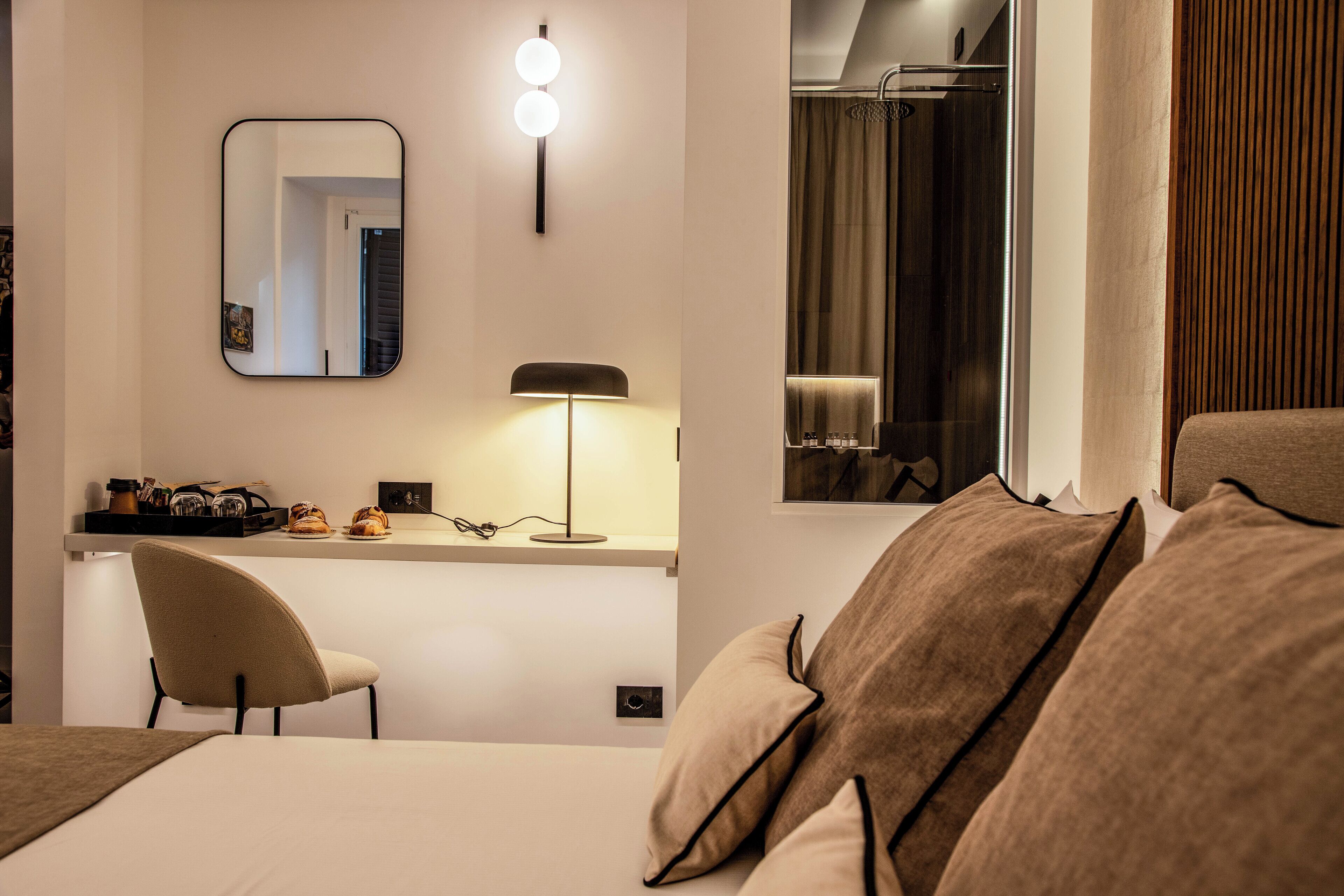 Una habitación de hotel moderna con una cama, un escritorio con una silla, un espejo, una lámpara y una ventana con cortinas.