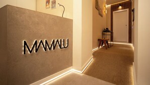 A reception area with a modern design, featuring a reception desk with illuminated letters, a small table, and a chair. - Mamalu - Corso Umberto (Naples)