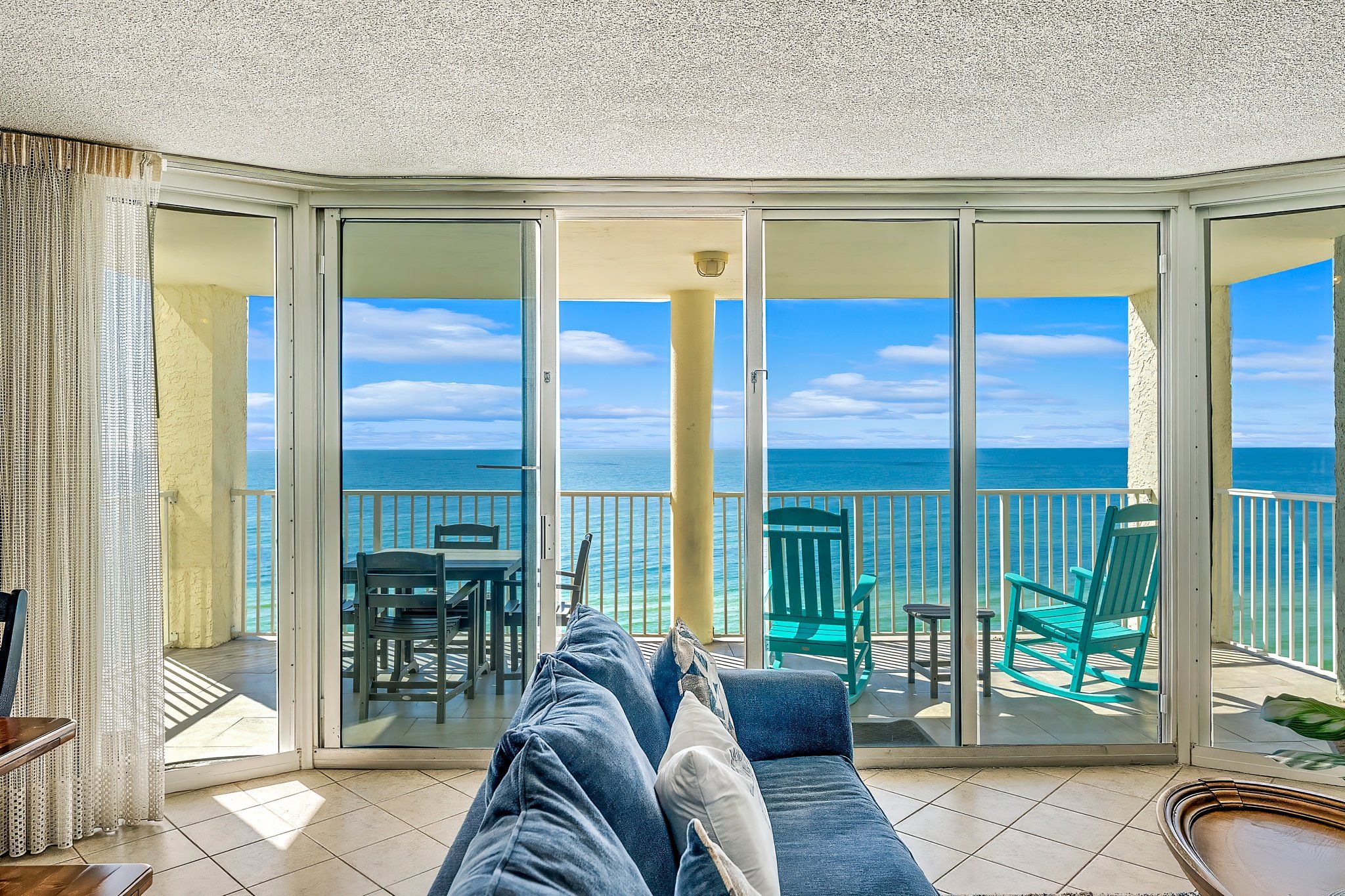A balcony with a view of the ocean, a sofa, and two green chairs.