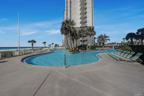 A swimming pool with lounge chairs, palm trees, and a tall building in the background.