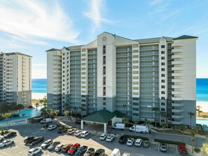 A high-rise hotel with multiple balconies, a swimming pool, and a parking lot.