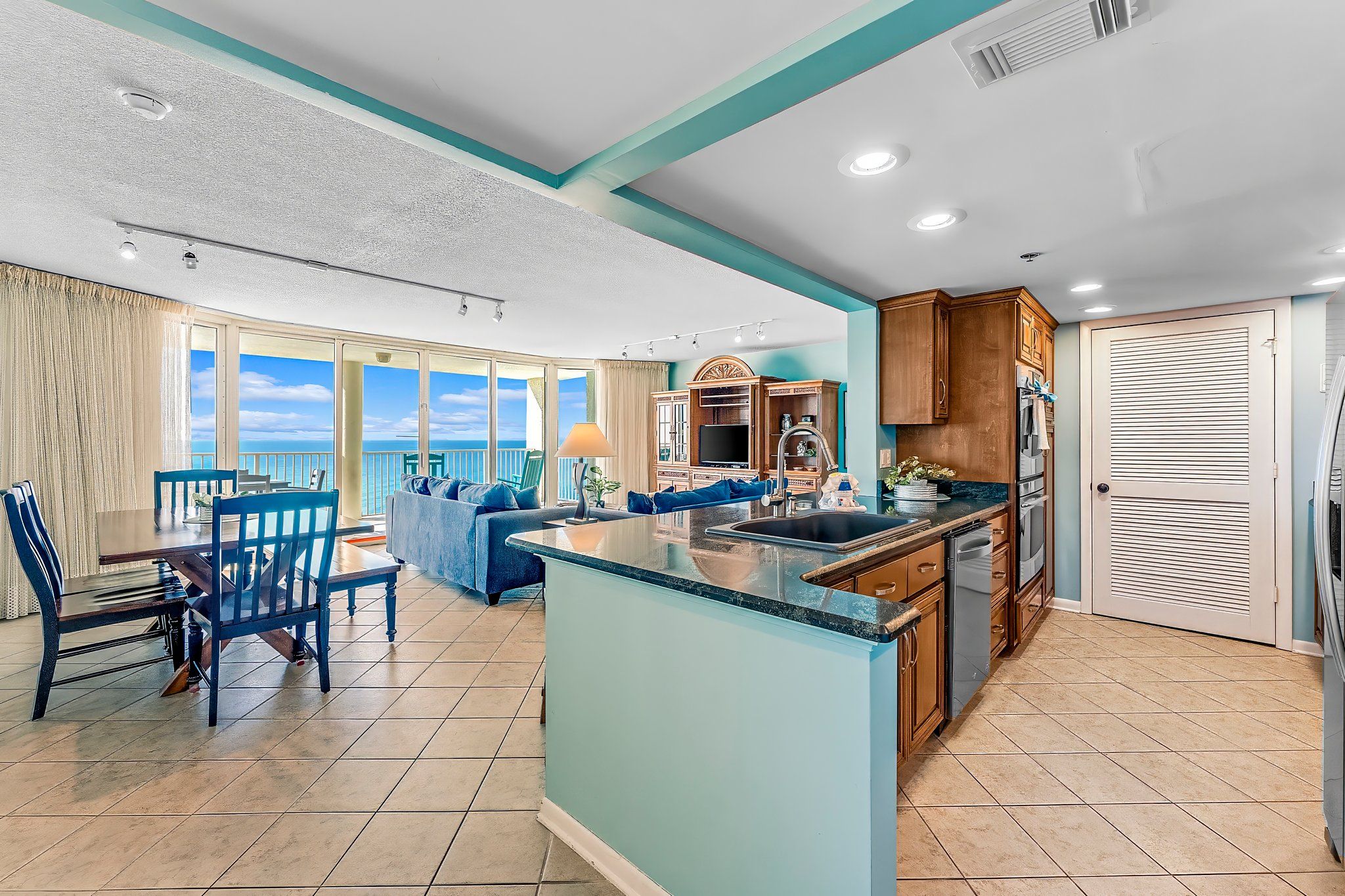 A spacious living area with a dining table and chairs, a blue sofa, and a kitchen with wooden cabinets and a large island.