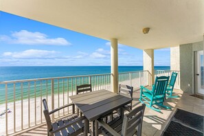 A balcony with a table and chairs, overlooking a beach and the ocean.