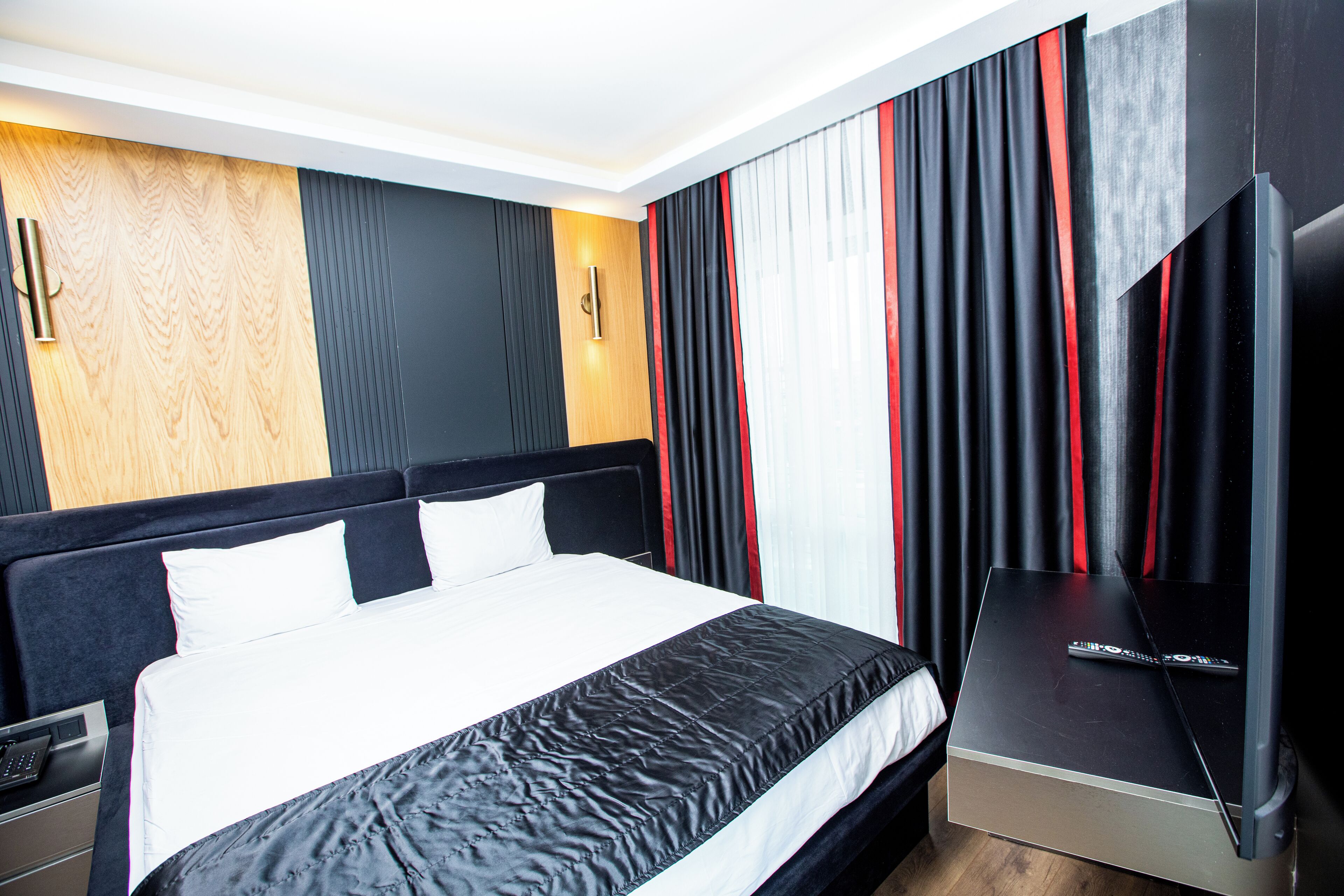 A modern hotel room with a large bed, a flat-screen TV, and a wooden accent wall.