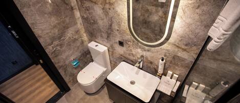 Een moderne badkamer met een marmeren wand, een grote spiegel, een wit wastafelmeubel en een toilet.