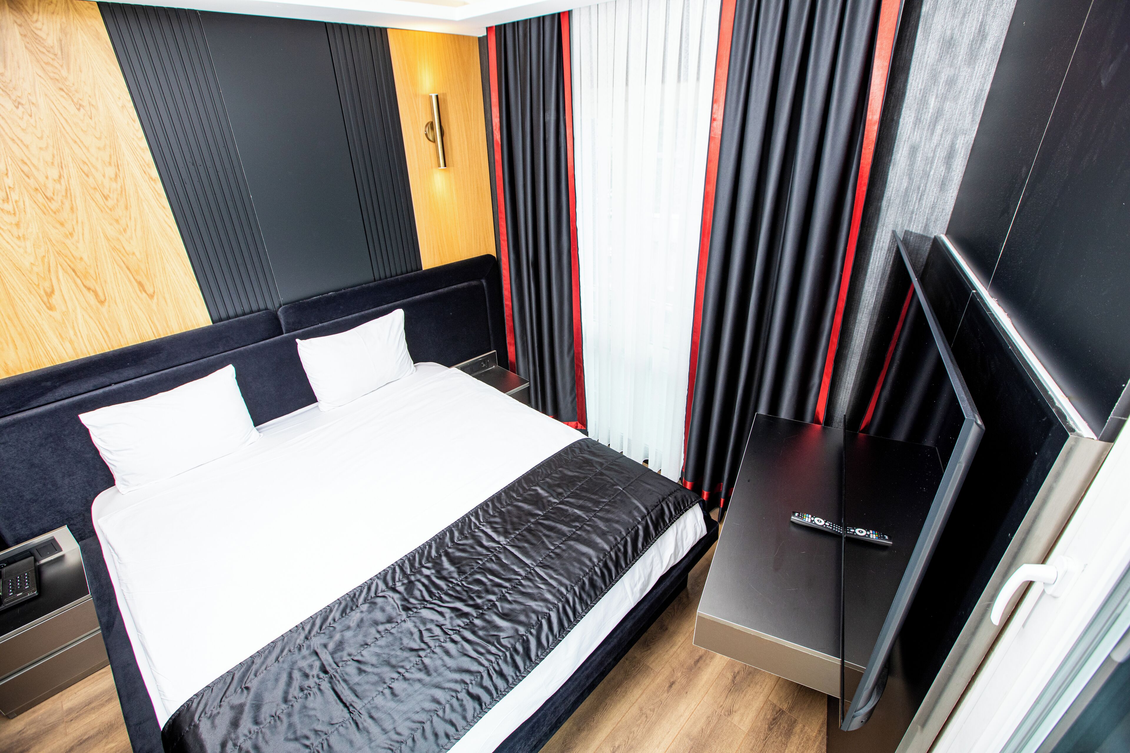 A modern hotel room with a large bed, a flat-screen TV, and a wooden accent wall.