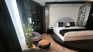 Un dormitorio moderno con una cama curvada, una mesita redonda pequeña, un sillón cómodo y una planta decorativa.