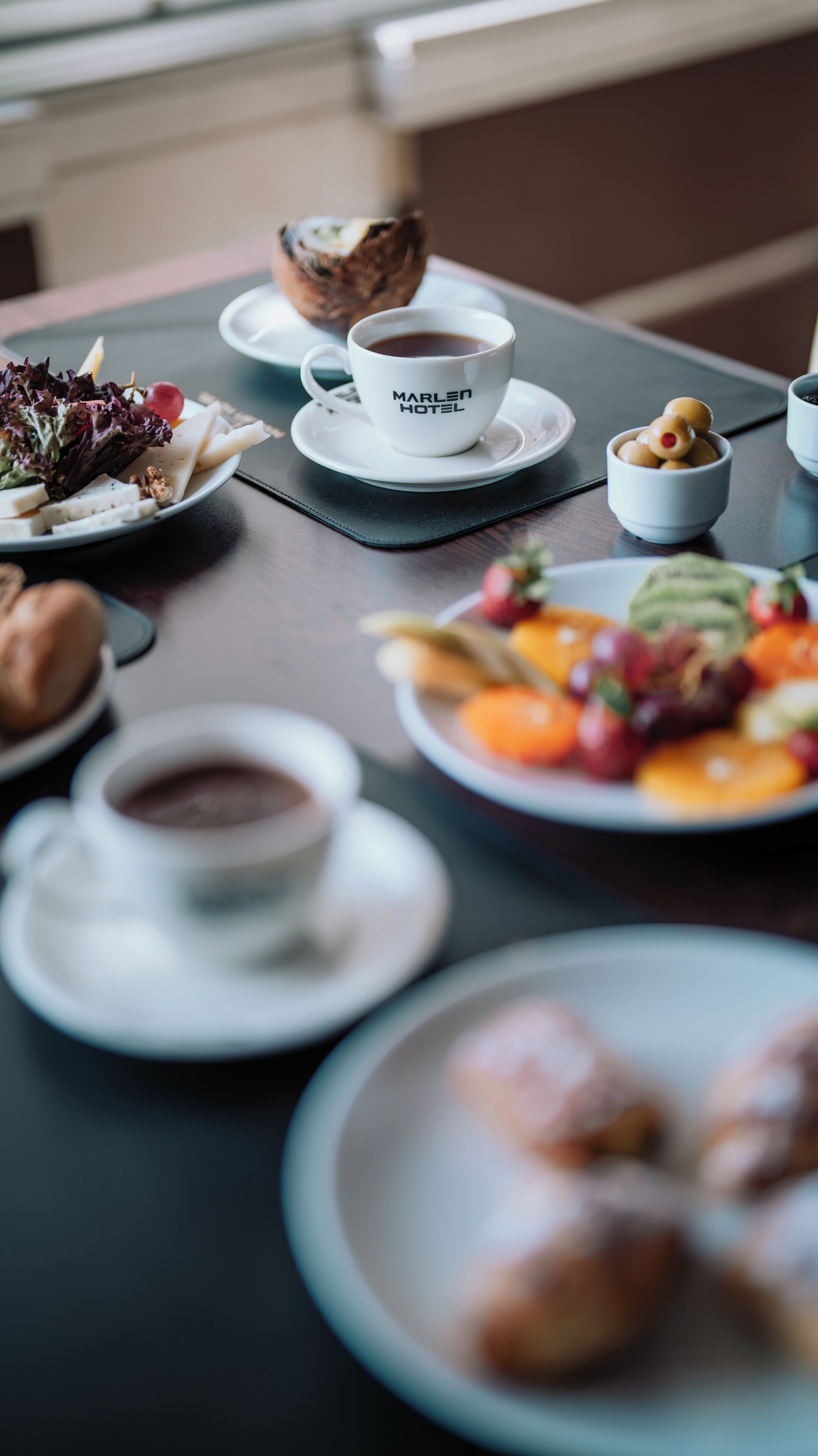 A table with a variety of food items including a plate of fruit, a cup of coffee, and pastries.