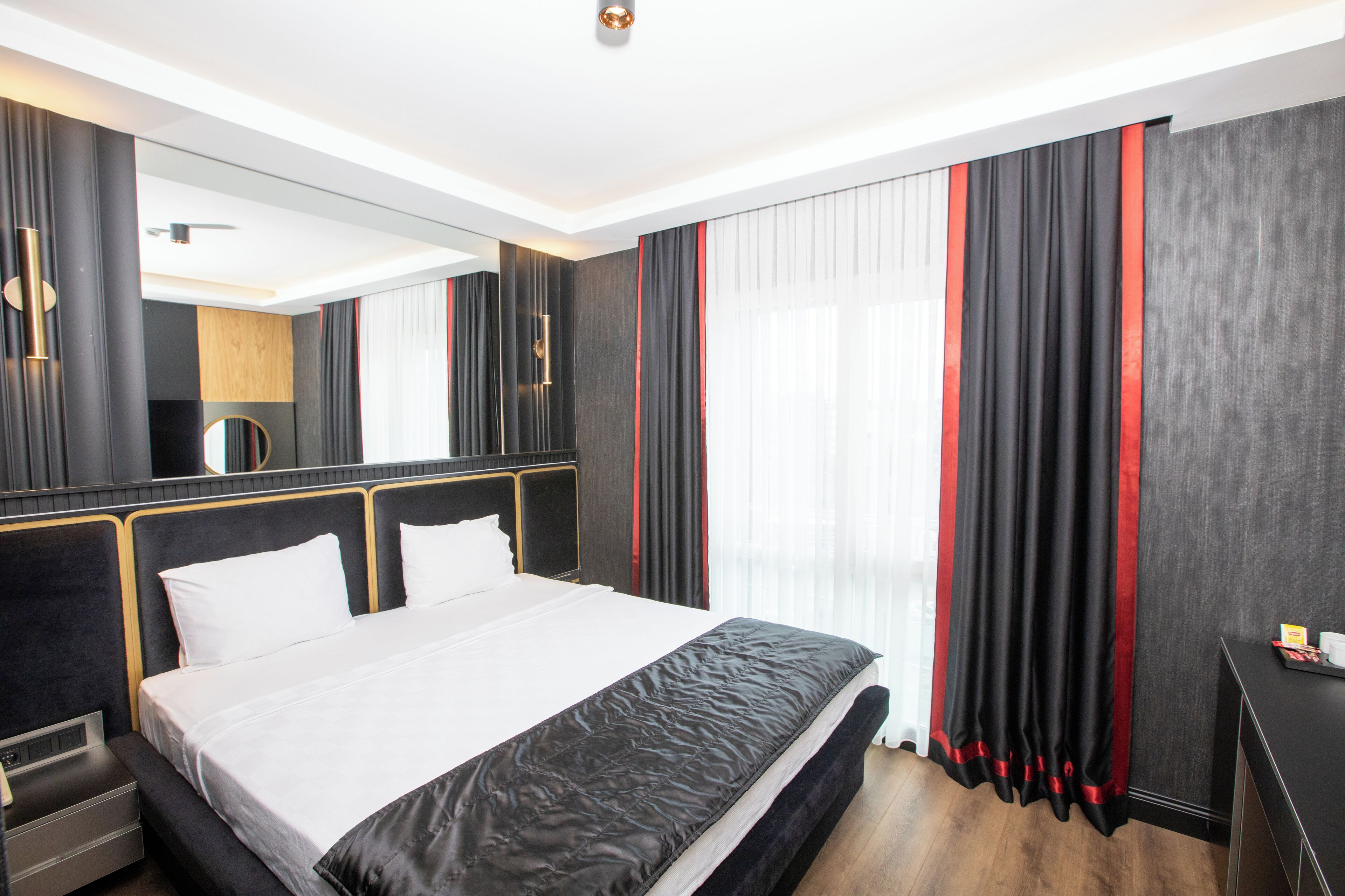 A modern hotel room with a large bed, a bedside table, a mirror, and a window with curtains.