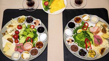 Two plates of food with various cheeses, meats, and vegetables, accompanied by small bowls of condiments and drinks on a table.