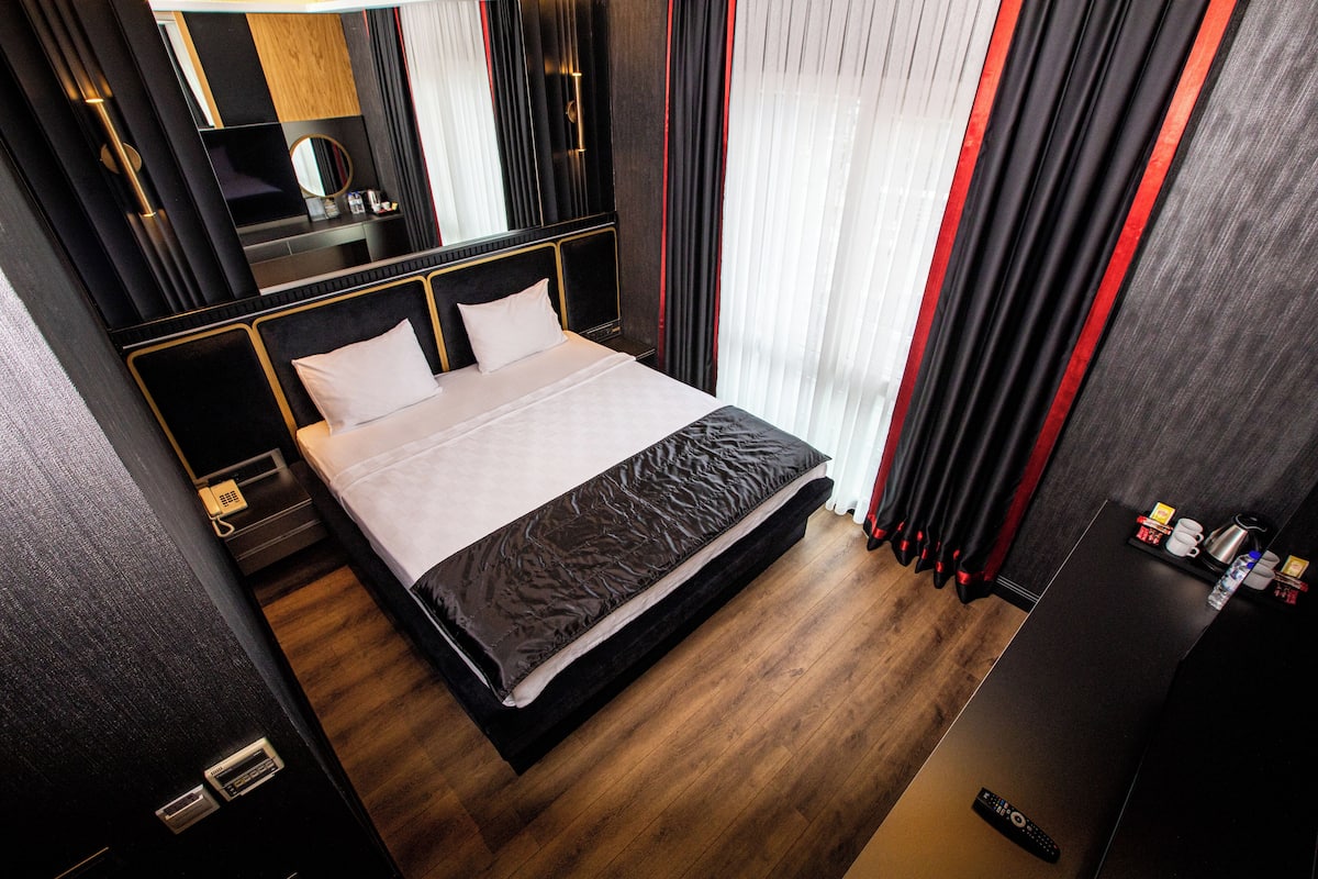 Quarto de hotel moderno com uma cama grande, mesa de cabeceira, espelho e guarda-roupa.