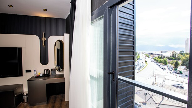 Habitación de hotel moderna con un ventanal grande, un televisor de pantalla plana, una pequeña kitchenette y vistas a una calle concurrida.