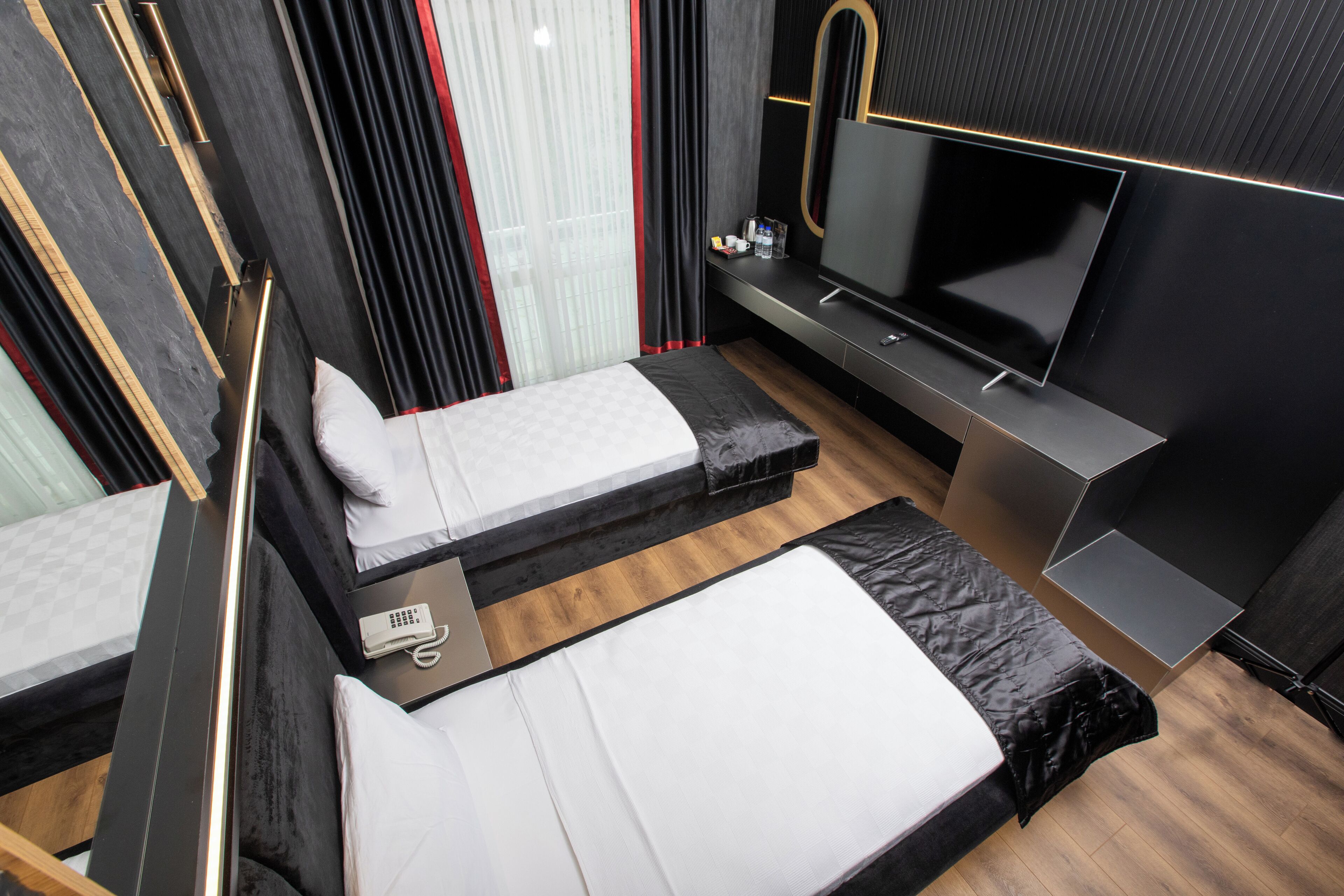 Camera d'albergo moderna con due letti singoli, una TV a schermo piatto, una piccola scrivania con telefono e un minibar.