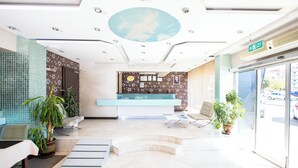 Un área de recepción con mostrador, asientos, plantas en macetas y vistas al exterior.